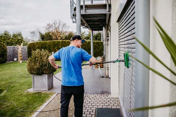 Gebäudereiniger mit blauem T-Shirt putzt Jalousie mit professionellem Reinigungsgerät von außen