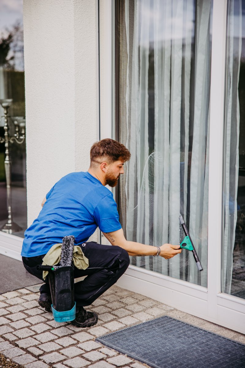 Reinigungskraft von cleanteam bei der Fensterreinigung in einem hellen Wohnzimmer